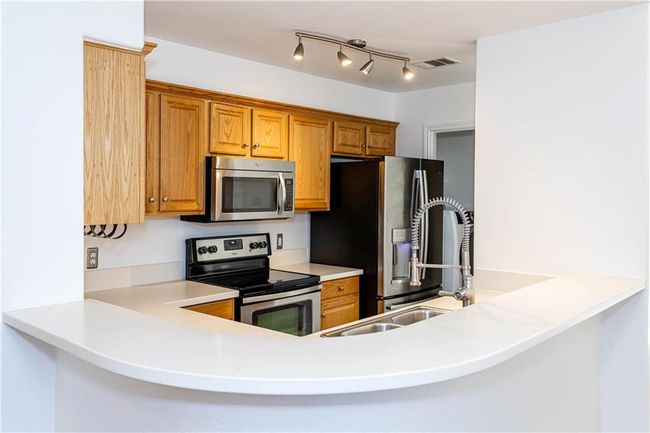 Kitchen with appliances with stainless steel finishes, a peninsula, light countertops, and brown cabinetry | Image 6