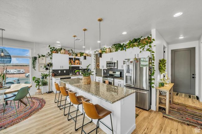 Kitchen featuring a kitchen island, light wood finished floors, open shelves, a breakfast bar area, and appliances with stainless steel finishes | Image 10