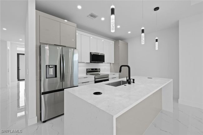 Kitchen featuring stainless steel appliances, a sink, light marble finish flooring, modern cabinets, and a center island with sink | Image 6
