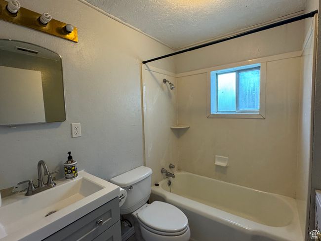 Full bathroom featuring a textured ceiling, toilet, shower / washtub combination, vanity, and a textured wall | Image 20
