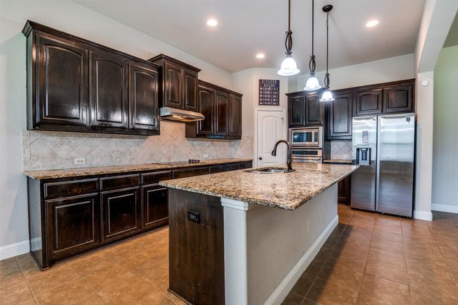 Kitchen featuring backsplash, appliances with stainless steel finishes, light tile patterned floors, light stone counters, and a kitchen island with sink | Image 9