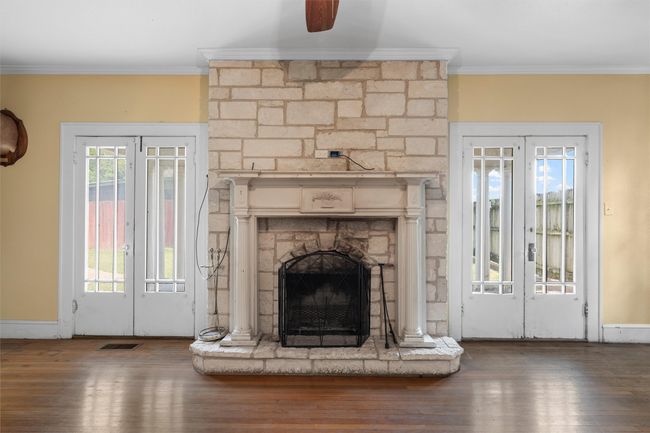 Unfurnished living room with french doors, crown molding, a fireplace, wood finished floors, and ceiling fan | Image 5