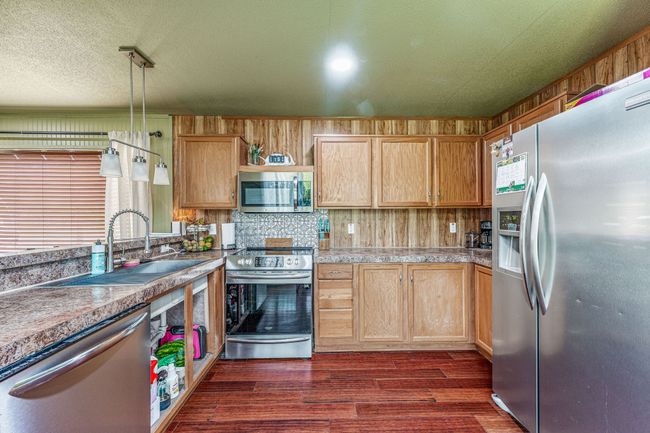 Kitchen featuring tile counters, dark wood finished floors, wooden walls, a sink, and appliances with stainless steel finishes | Image 23