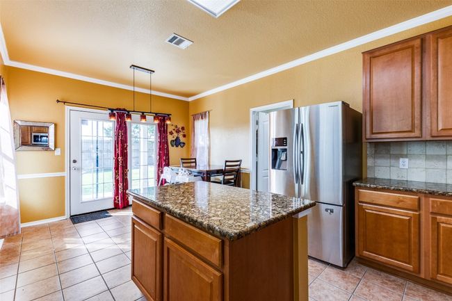 Kitchen featuring appliances with stainless steel finishes, brown cabinets, a center island, light tile patterned flooring, and crown molding | Image 13
