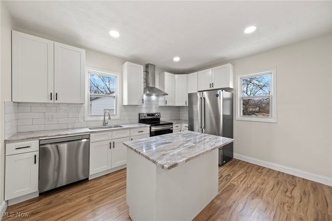 Kitchen featuring wall chimney exhaust hood, white cabinetry, sink, and appliances with stainless steel finishes | Image 12
