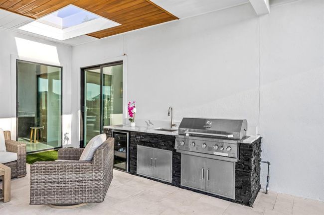 This covered outdoor kitchen is a chef’s dream, featuring a built-in stainless steel grill, sink, and mini fridge. A sleek skylight above brings in natural light, creating the perfect spot for cooking and entertaining in any season. | Image 41