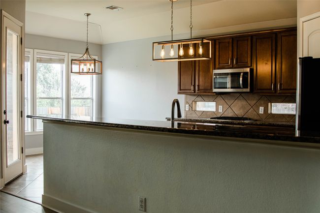 Kitchen with stainless steel microwave, backsplash, dark brown cabinetry, decorative light fixtures, and freestanding refrigerator | Image 12