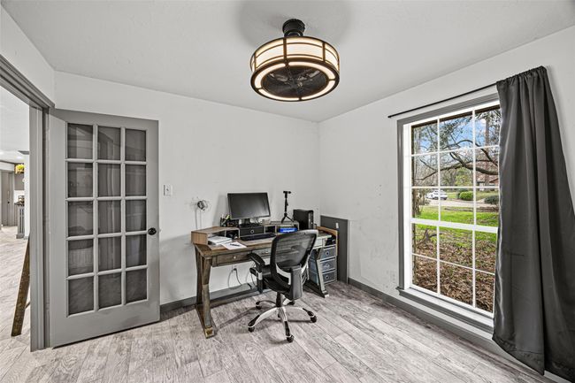 Bright home office with modern lighting and a large window offering natural light and garden views. The room includes a stylish desk setup and glass panel door. Home office can be easily converted into a playroom or media lounge. | Image 12