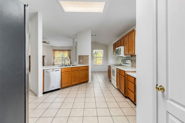 Kitchen with stainless steel appliances, a sink, light countertops, brown cabinets, and vaulted ceiling | Image 14