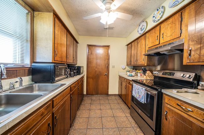 Kitchen featuring stainless steel electric range, under cabinet range hood, a textured ceiling, light countertops, and a ceiling fan | Image 11
