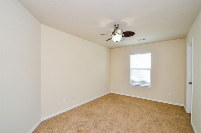 This secondary bedroom features neutral walls, carpeted flooring, a ceiling fan with light, and a window with blinds offering natural light. It's a versatile space suitable for a bedroom or office. | Image 26