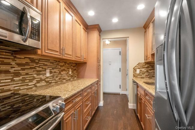 Kitchen with tasteful backsplash, baseboards, light stone counters, dark wood-style floors, and stainless steel appliances | Image 10