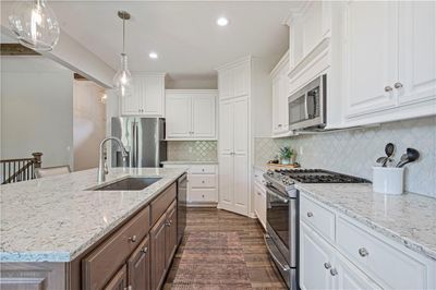 Kitchen with appliances with stainless steel finishes, white cabinetry, sink, and a center island with sink | Image 3