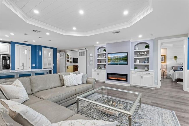 Living area featuring a raised ceiling, a barn door, recessed lighting, light wood-style floors, and built in shelves | Image 4