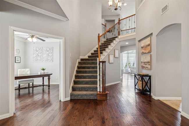 Stairs with ceiling fan with notable chandelier, dark hardwood / wood-style floors, crown molding, and a high ceiling | Image 3