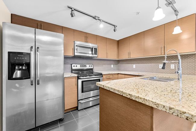 Kitchen featuring light stone countertops, a sink, appliances with stainless steel finishes, dark tile patterned floors, and tasteful backsplash | Image 9