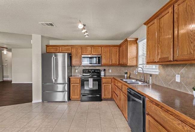 Kitchen with appliances with stainless steel finishes, brown cabinetry, tasteful backsplash, dark countertops, and light tile patterned flooring | Image 22