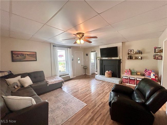 Living area featuring ceiling fan, wood finished floors, a fireplace with raised hearth, and a drop ceiling | Image 8