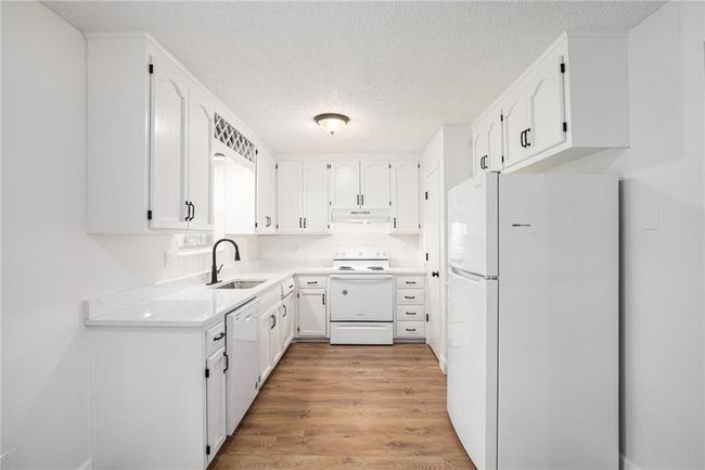 Kitchen featuring white appliances, a sink, under cabinet range hood, a textured ceiling, and white cabinets | Image 8