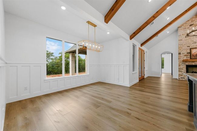 Unfurnished living room with high vaulted ceiling, light hardwood / wood-style floors, beam ceiling, a fireplace, and an inviting chandelier | Image 9