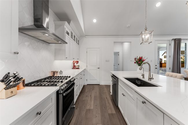 Kitchen featuring wall chimney range hood, stainless steel appliances, decorative backsplash, white cabinetry, and light countertops | Image 8