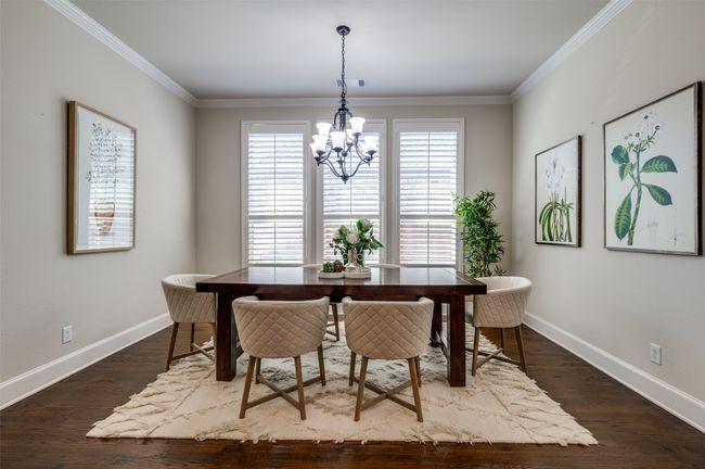 The formal dining room is bathed in natural light, thanks to three large windows accented with plantation shutters. Thick baseboards and crown molding add an elegant touch, enhancing the refined atmosphere of the space. | Image 7