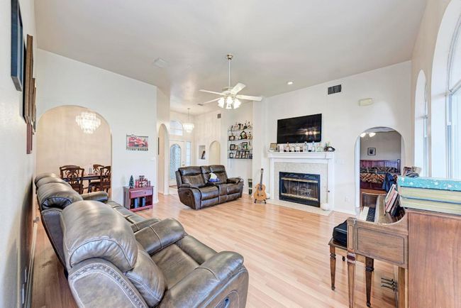Living area featuring arched walkways, ceiling fan, a fireplace with flush hearth, and wood finished floors | Image 12
