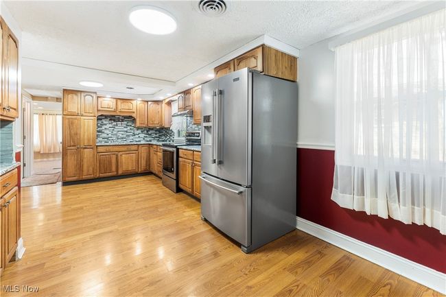 Kitchen featuring tasteful backsplash, light wood-style flooring, visible vents, stainless steel appliances, and brown cabinetry | Image 17
