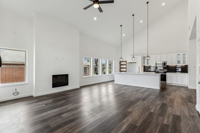 Unfurnished living room featuring high vaulted ceiling, a ceiling fan, a glass covered fireplace, dark wood-type flooring, and recessed lighting | Image 11
