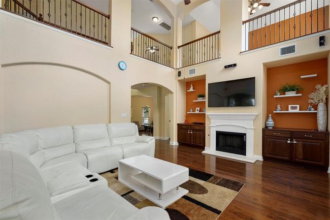 Living room featuring a ceiling fan, dark wood finished floors, arched walkways, a high ceiling, and a fireplace with raised hearth | Image 11