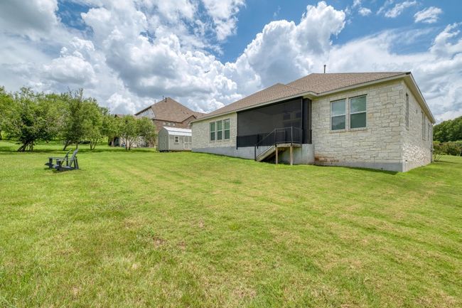 Rear view of house featuring a storage shed, stone siding, a yard, and roof with shingles | Image 30