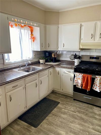 Kitchen featuring white cabinets, backsplash, light wood-type flooring, stainless steel electric range oven, and sink | Image 2