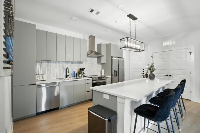 Kitchen featuring appliances with stainless steel finishes, wall chimney range hood, gray cabinetry, a breakfast bar, and a kitchen island | Image 7