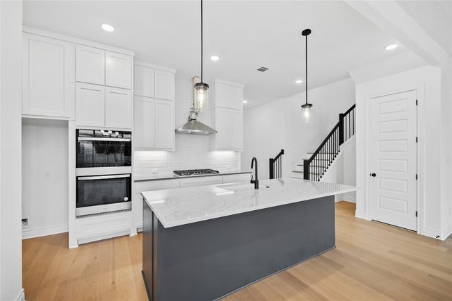 Kitchen featuring light wood-type flooring, tasteful backsplash, white cabinetry, light stone countertops, and double oven | Image 26