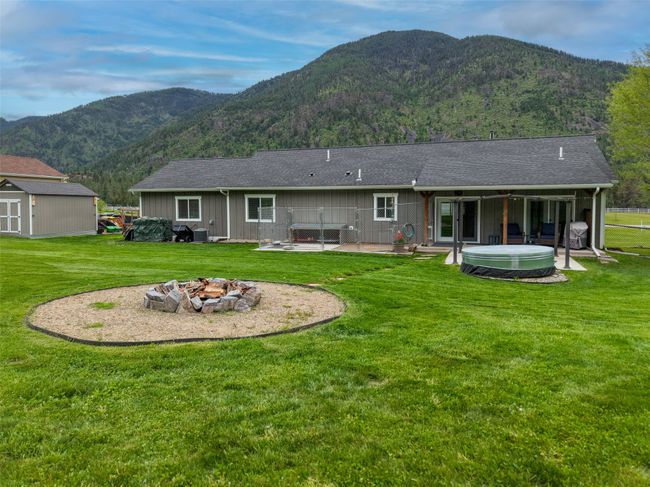 Back of house featuring a hot tub, an outdoor fire pit, a mountain view, a yard, and a patio | Image 41