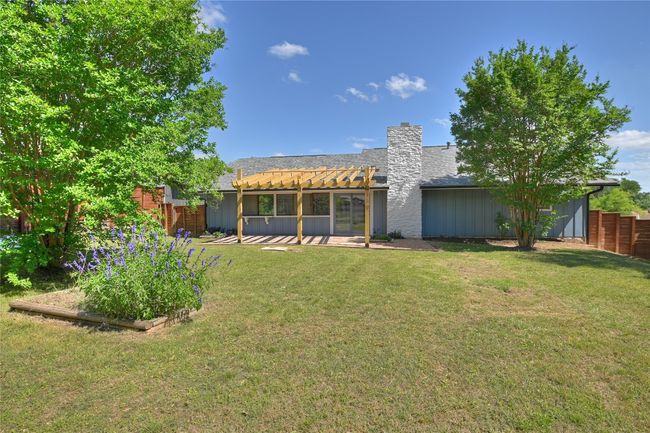 Rear view of house with a pergola, a chimney, board and batten siding, a patio area, and vegetable garden beds | Image 22