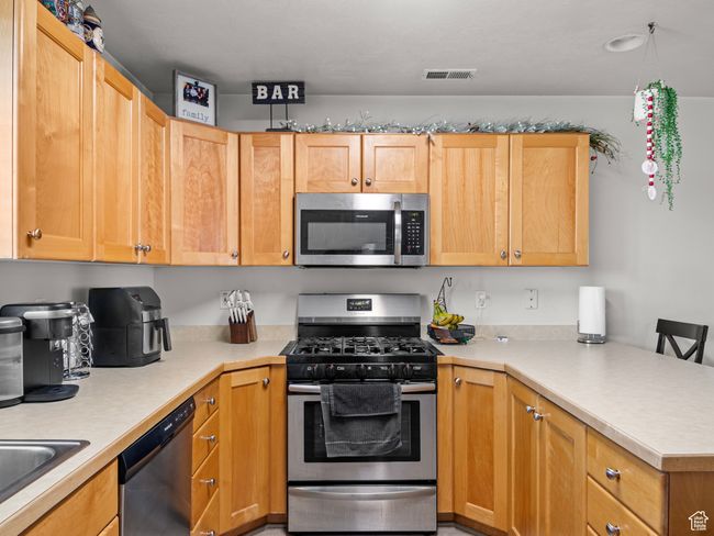 Kitchen featuring a breakfast bar, sink, light brown cabinetry, kitchen peninsula, and stainless steel appliances | Image 9