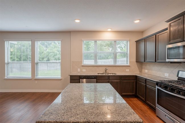 Kitchen featuring appliances with stainless steel finishes, light stone counters, backsplash, and wood finished floors | Image 5