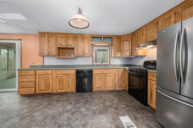 Kitchen featuring stone finish flooring, black appliances, under cabinet range hood, and visible vents | Image 17