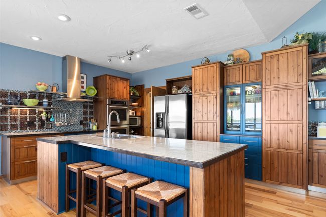 Kitchen featuring appliances with stainless steel finishes, wall chimney exhaust hood, light hardwood / wood-style floors, and an island with sink | Image 10