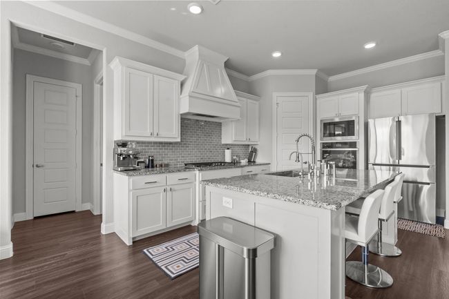 Kitchen featuring appliances with stainless steel finishes, premium range hood, white cabinets, dark wood finished floors, and backsplash | Image 8