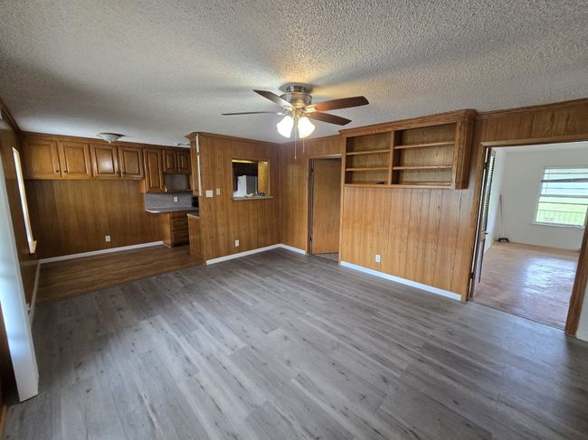 Unfurnished living room featuring a ceiling fan, wood walls, wood finished floors, and a textured ceiling | Image 23
