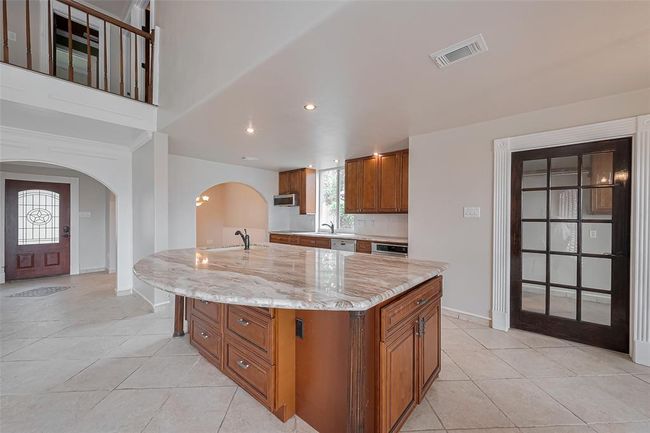 A wide-open kitchen layout offers clear views to the living room and front entry. Arched transitions and warm wood cabinetry complement the sophisticated marble countertops, while the glass-paneled pantry door adds a touch of charm. | Image 15