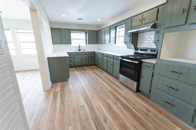 Kitchen with light wood finished floors, under cabinet range hood, decorative backsplash, stainless steel range with electric stovetop, and green cabinetry | Image 10