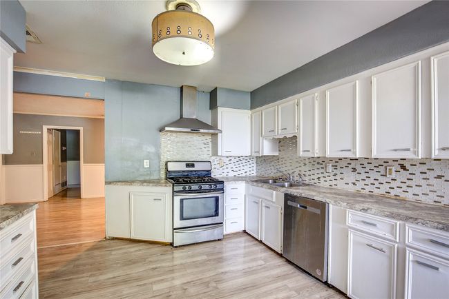 Kitchen featuring appliances with stainless steel finishes, wall chimney range hood, a sink, light wood-style floors, and white cabinetry | Image 6
