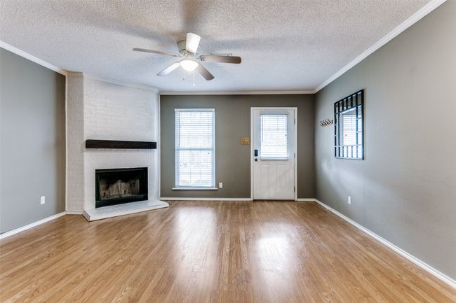 Unfurnished living room with a textured ceiling, a ceiling fan, light wood finished floors, crown molding, and a fireplace | Image 5