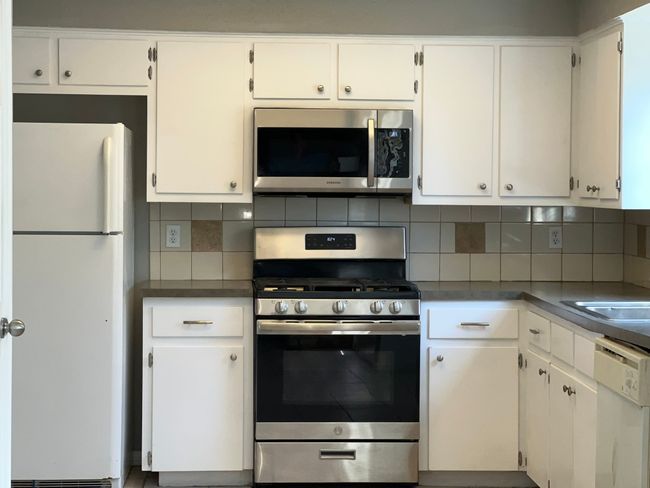 Kitchen with stainless steel appliances, tasteful backsplash, white cabinets, and dark countertops | Image 9