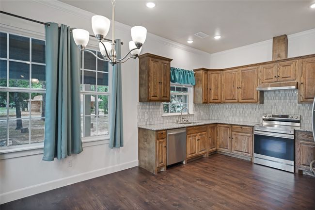 Kitchen with stainless steel appliances, under cabinet range hood, backsplash, light stone countertops, and ornamental molding | Image 10