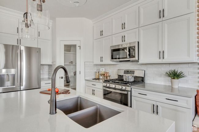Kitchen with appliances with stainless steel finishes, white cabinets, tasteful backsplash, light countertops, and pendant lighting | Image 35