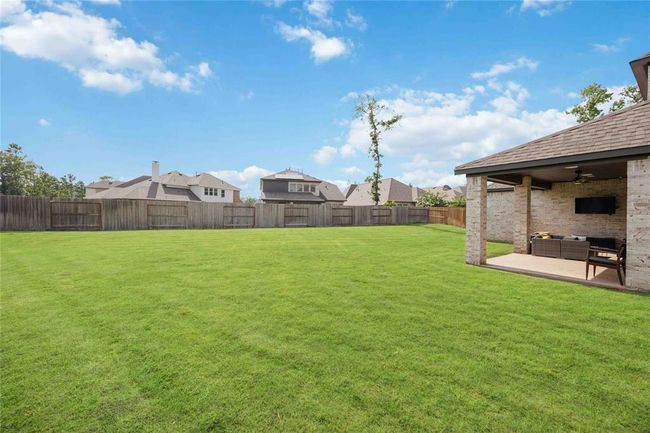 Spacious backyard with lush grass, enclosed by a wooden fence for privacy. Features a covered patio area with outdoor seating, ideal for relaxation and entertaining. | Image 36